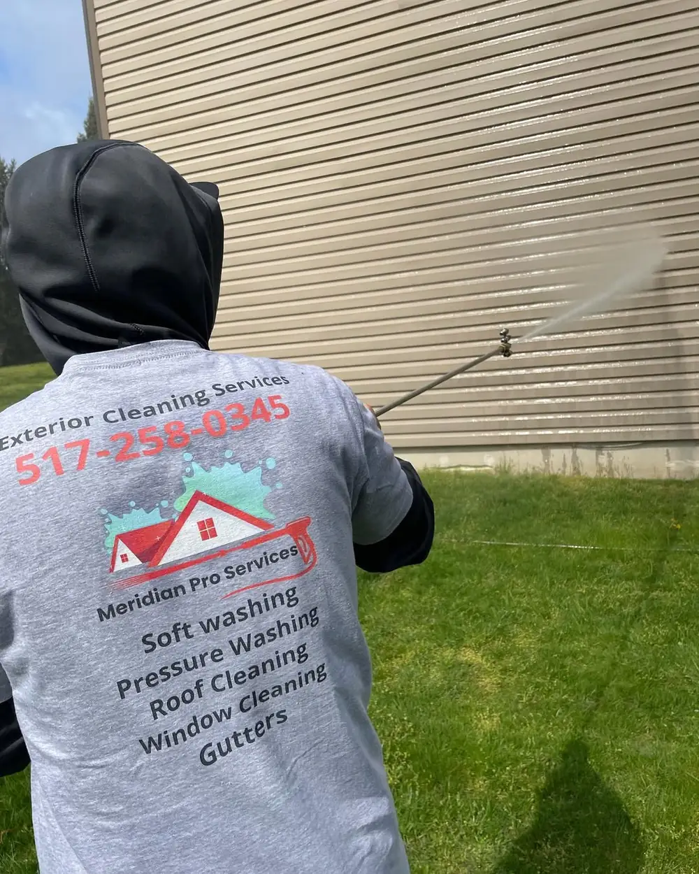 Meridian Pro Services technician soft washing home siding in Holt, MI
