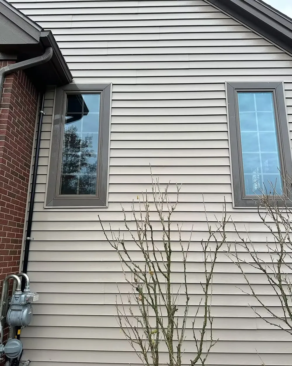 Clean cream vinyl siding and windows on the side of a brick-cornered home in Dewitt, MI