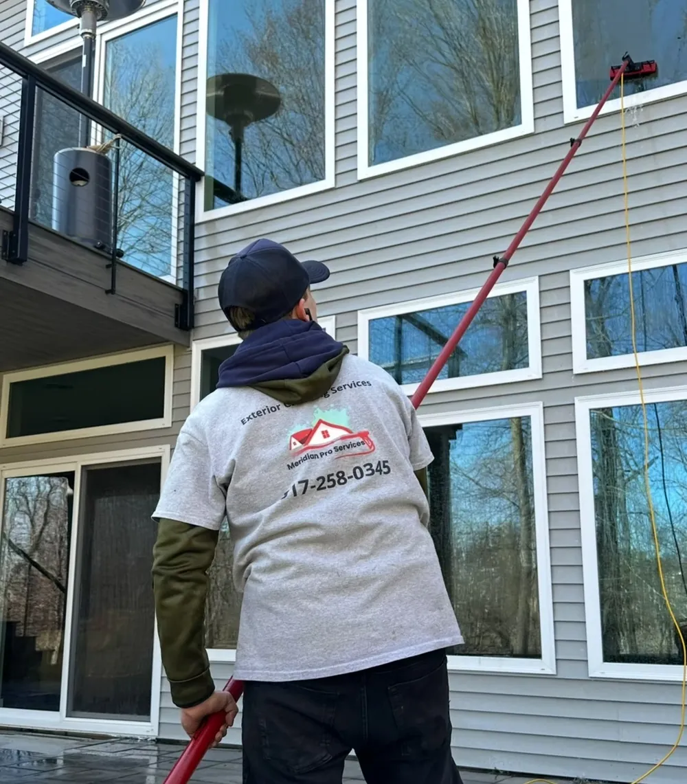 Technician cleaning home windows with a water-fed pole in Okemos, MI