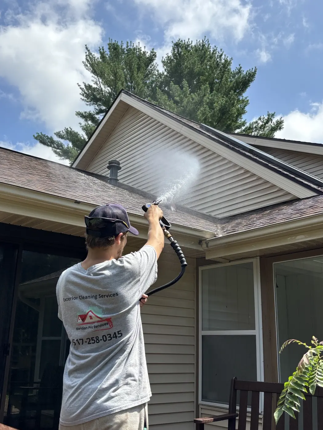 Meridian Pro Services technician soft washing the siding and gable of a home with a low-pressure spray